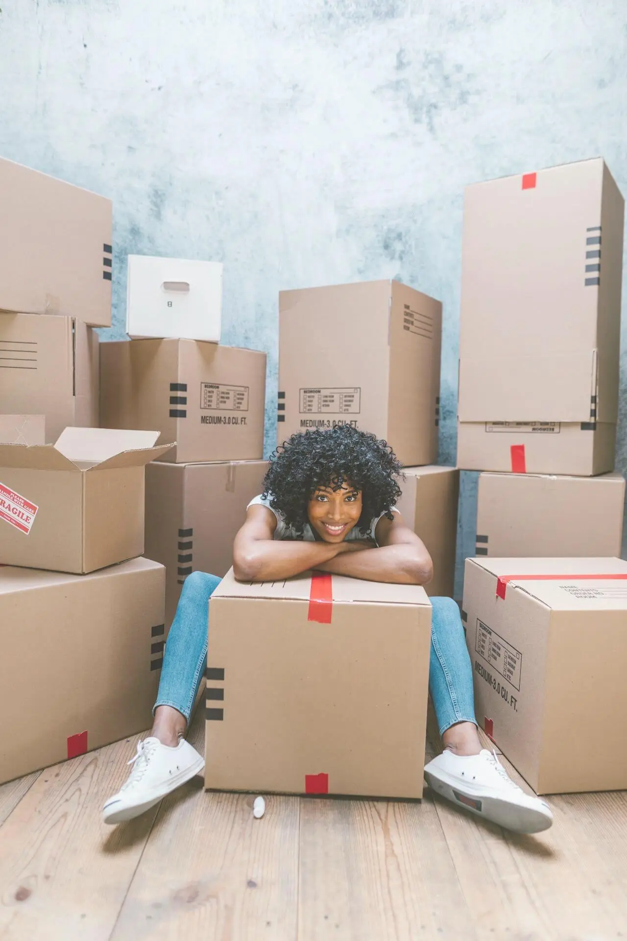 Young adult surrounded by moving boxes while unpacking after moving out for the first time in their 20s.