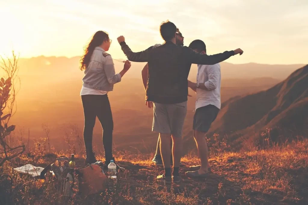 Three young adults standing on a mountain at sunset, laughing and enjoying the view, symbolizing freedom, friendship, and the wealth of experiences in your 20s.