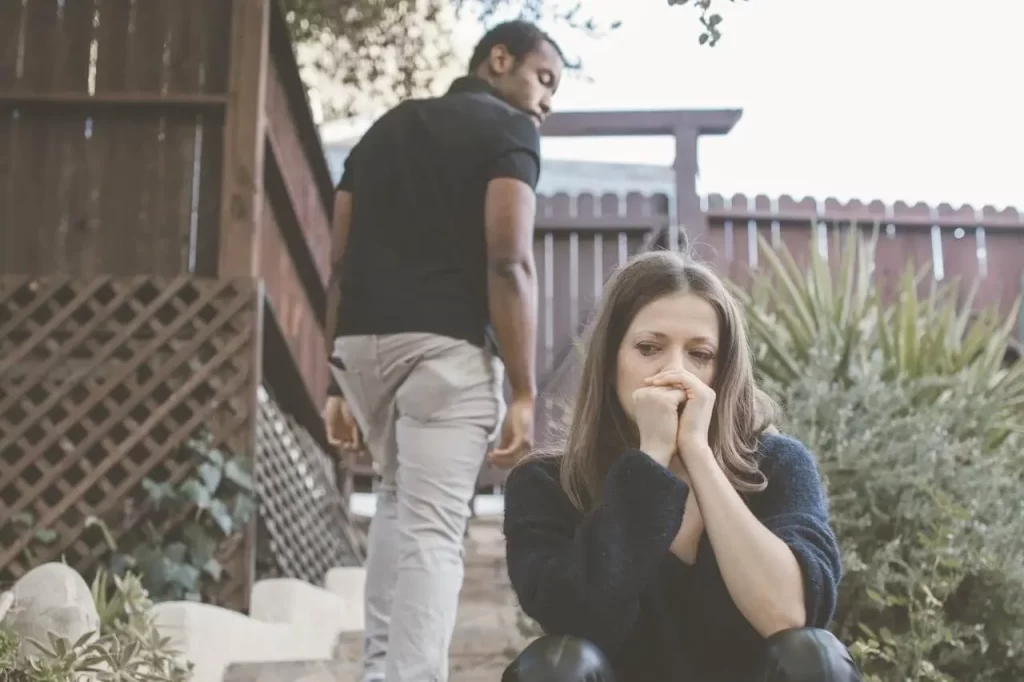 Woman sitting on outdoor steps looking heartbroken while a man walks away in the background, symbolizing the end of a relationship.