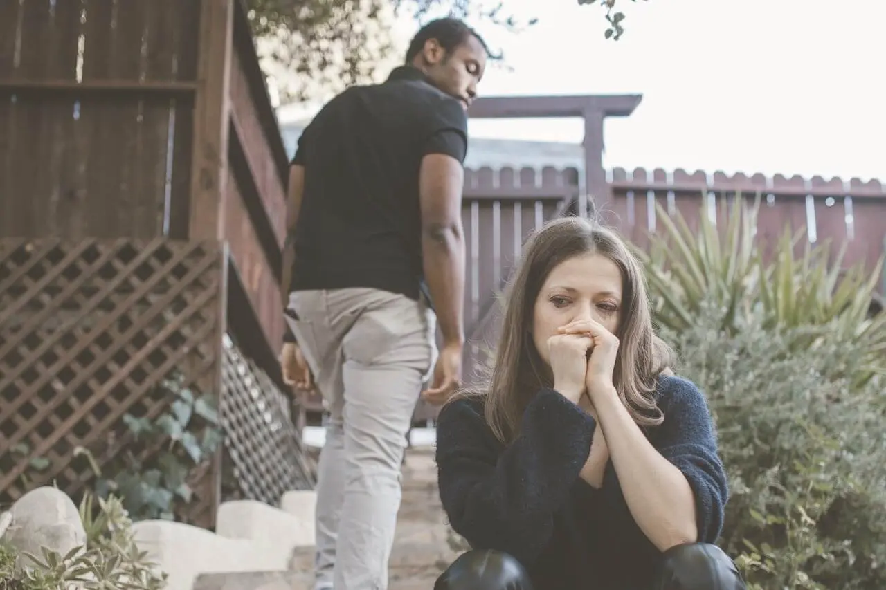 Woman sitting on outdoor steps looking heartbroken while a man walks away in the background, symbolizing the end of a relationship.
