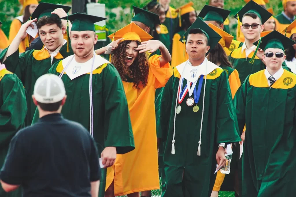 Group of college graduates wearing green and gold caps and gowns walking at a graduation ceremony.